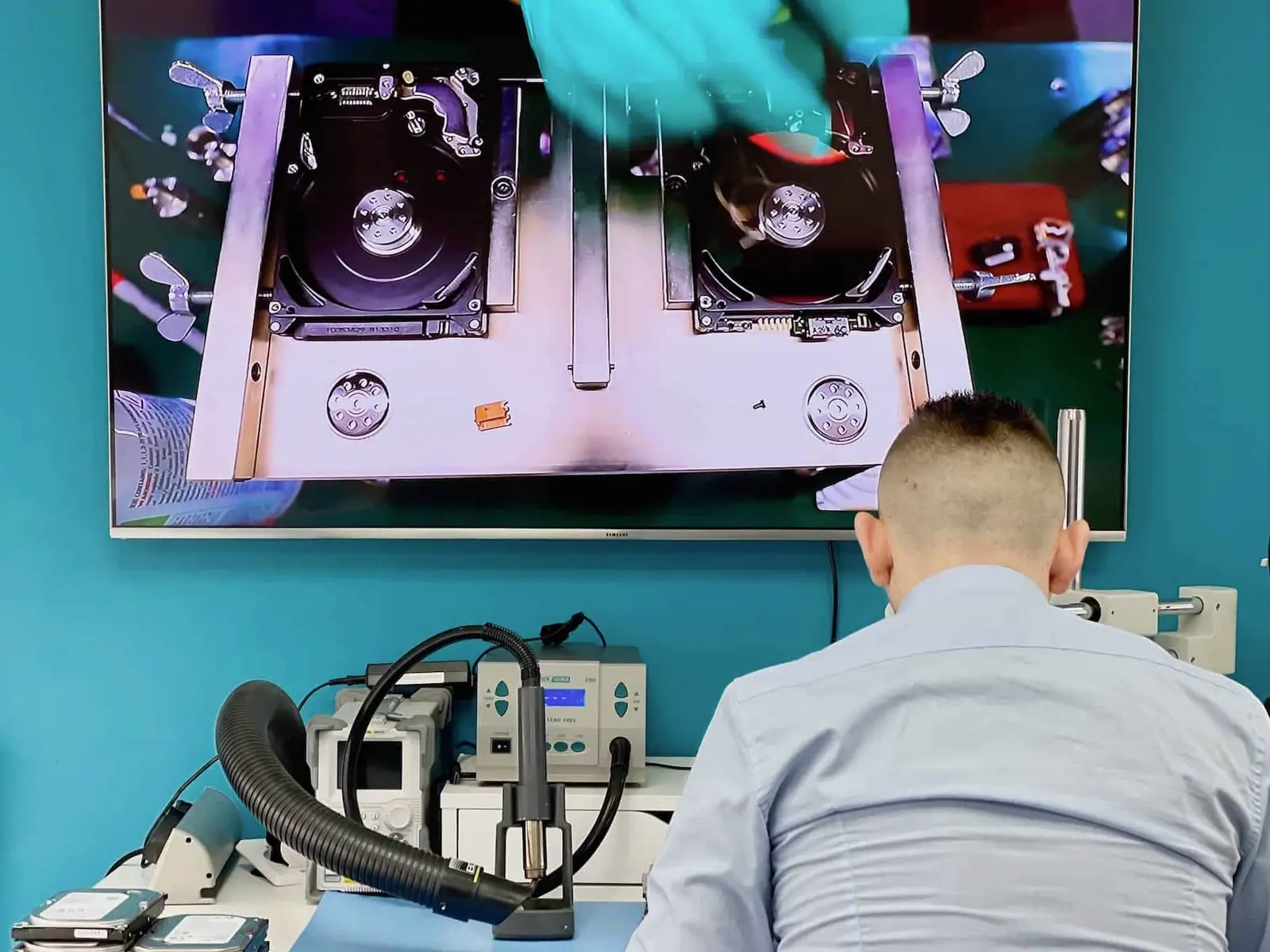 A technician carrying out a hard drive head transfer while the work is magnified on a laboratory display
