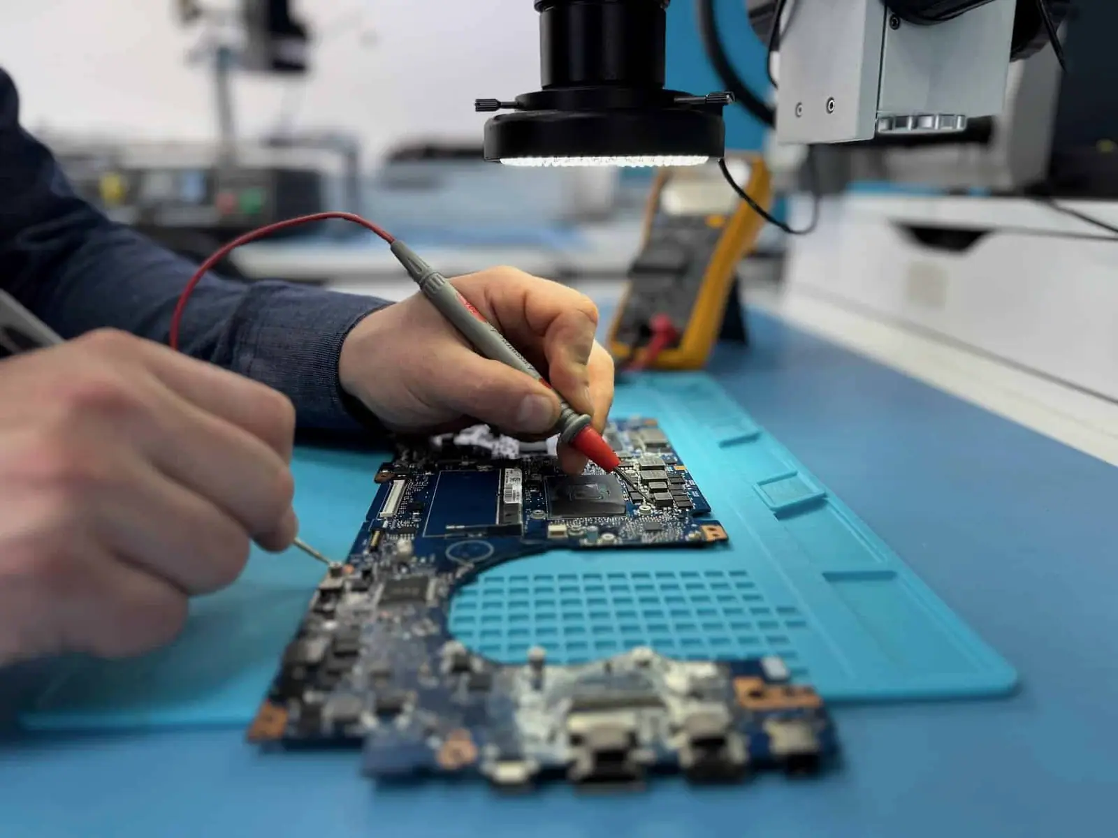 Multimeter probes tracing a fault across a laptop logic board