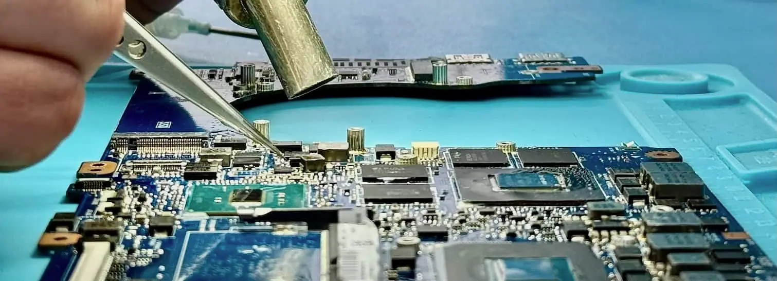 A hot-air nozzle over a laptop logic board during component removal