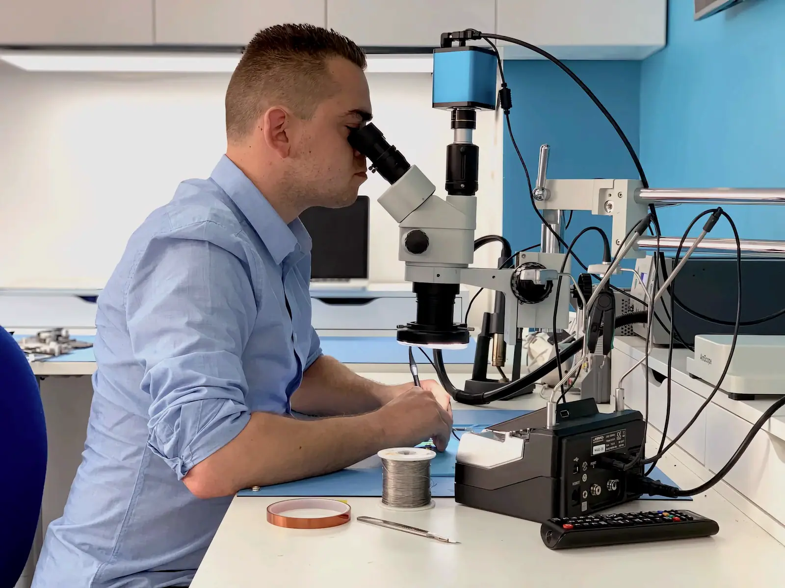 A technician working at a stereo microscope with a soldering iron and fine tools
