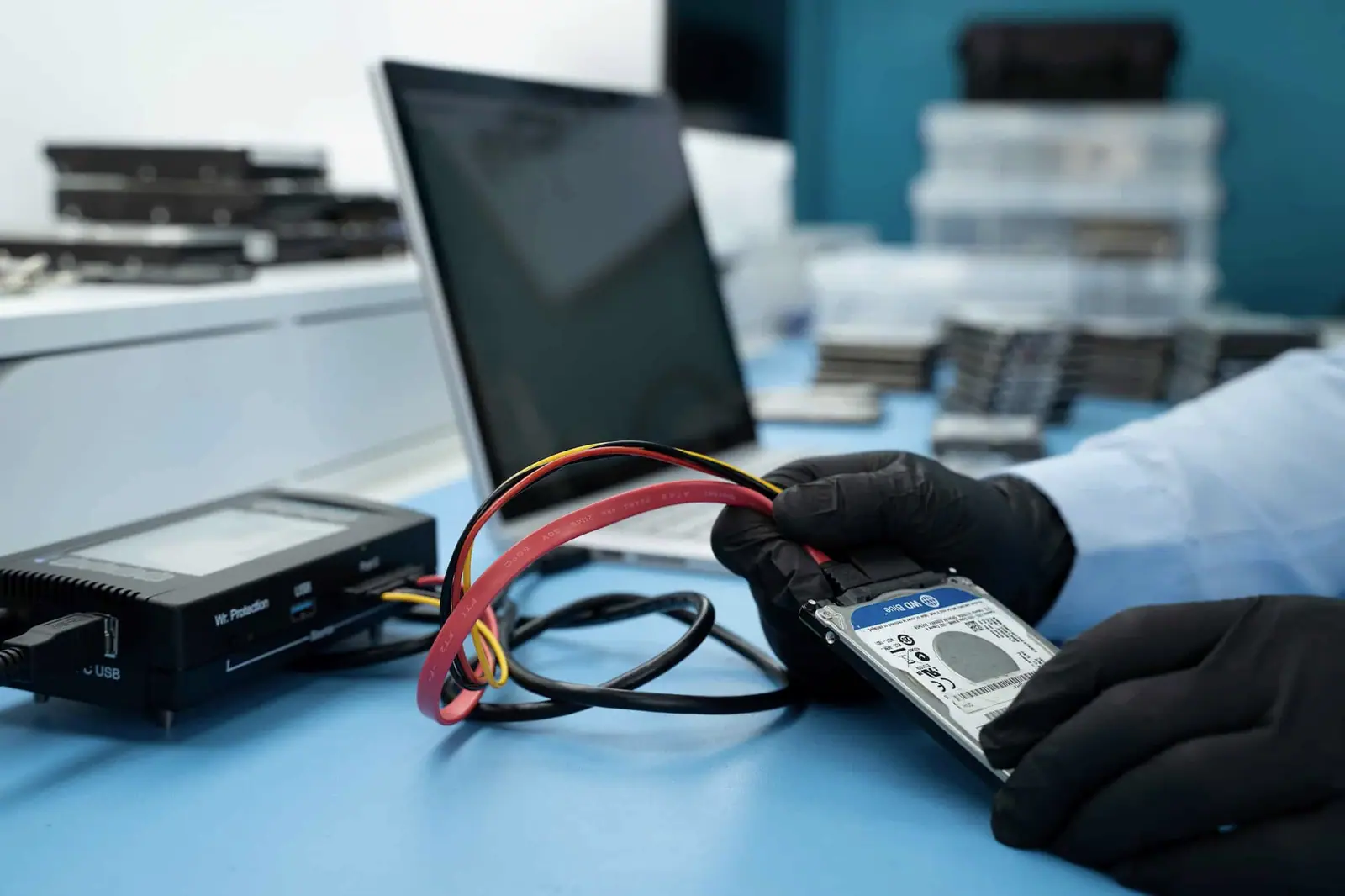 Gloved hands connecting a solid-state drive to diagnostic hardware on a lab bench