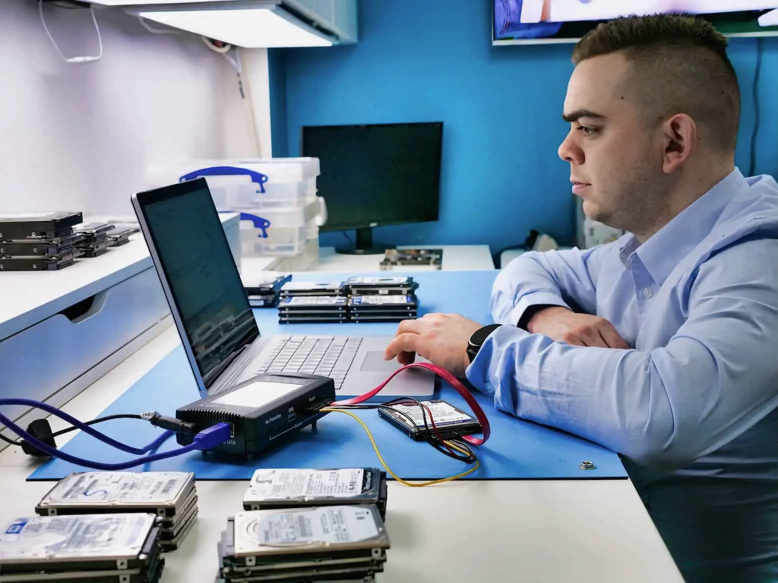 A technician running drive diagnostics at a bench stacked with hard drives